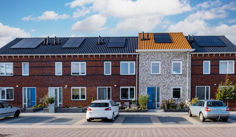 Straat met huizen met zonnepanelen op het dak en een elektrische auto aan de straat geparkeerd